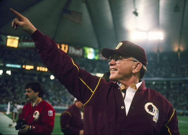 Washington Redskins head coach Joe Gibbs points from the sideline during the 1991 NFL season, wearing a team jacket and cap at the Metrodome.